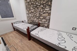 Ein Zimmer mit zwei Einzelbetten, einer Steinwand, einem Fenster und einem Holzboden.