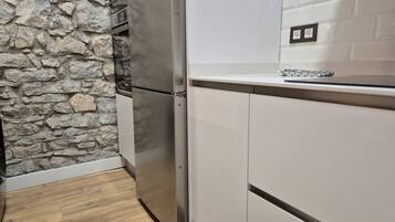 Una cocina con pared de piedra, refrigerador de acero inoxidable y armarios blancos.