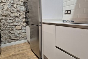 Une cuisine avec un mur en pierre, un réfrigérateur en acier inoxydable et des armoires blanches.