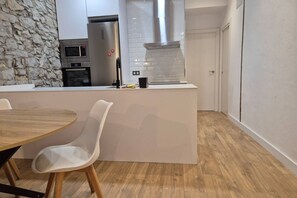 A modern kitchen with a stone accent wall, a built-in oven, and a stainless steel refrigerator.