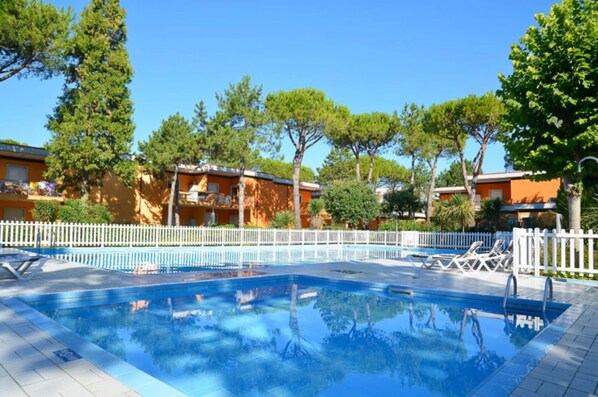 A swimming pool with lounge chairs and a white fence.