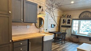 Una cocina rústica con armarios de madera, un refrigerador de acero inoxidable, una encimera de madera, un fregadero y una ventana con vistas a árboles.
