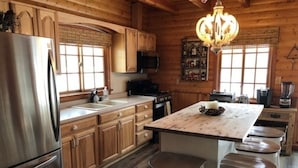 Cocina de estilo cabaña de madera con una isla central, taburetes de bar, un refrigerador y una araña.