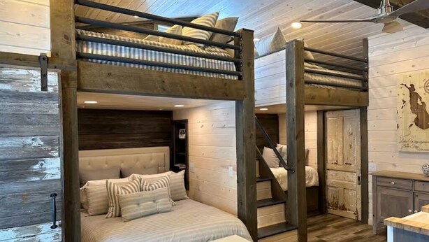 Habitación con literas, techo de madera, escalera y un pequeño escritorio.
