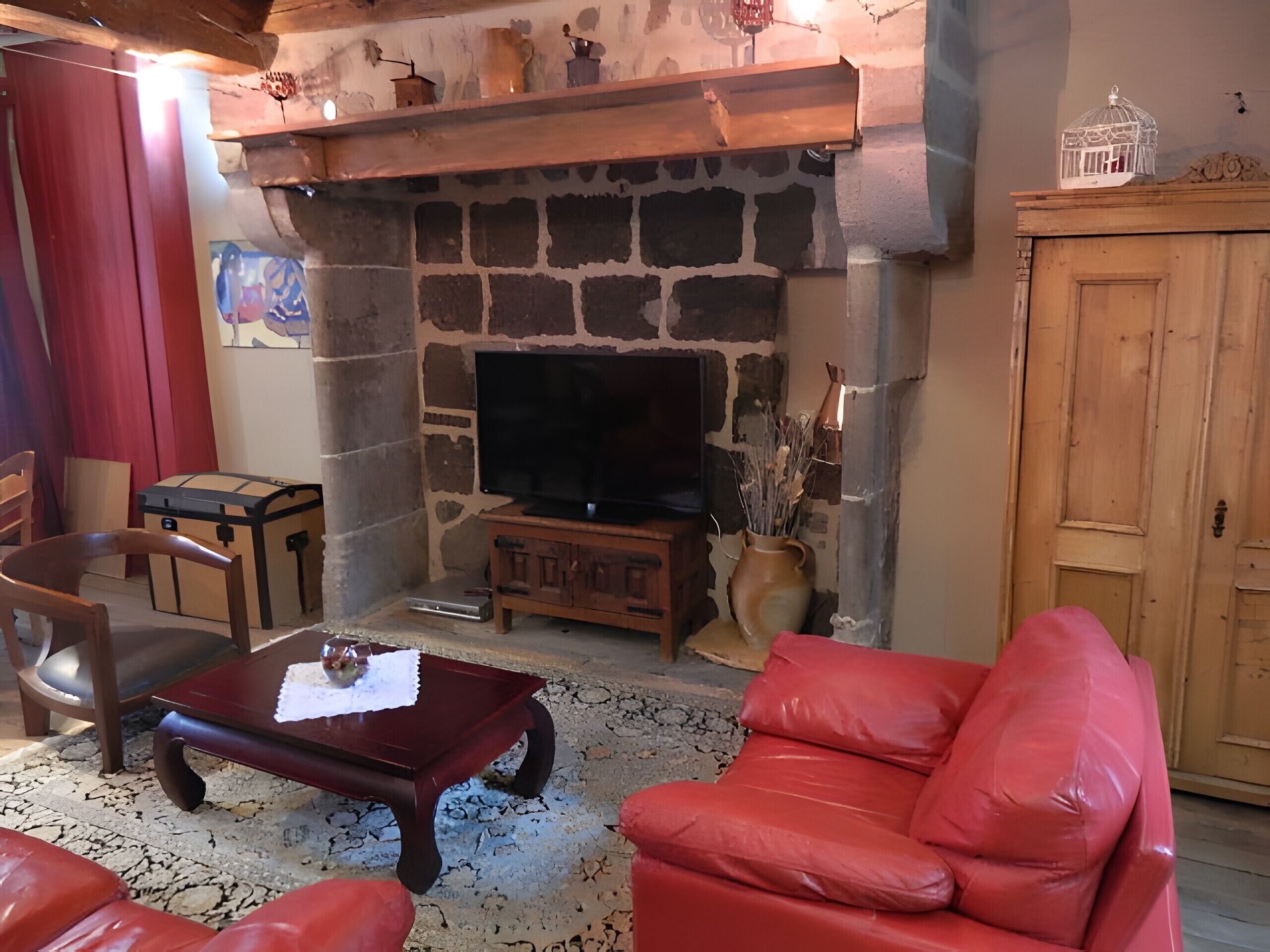 Ein Wohnzimmer mit Kamin aus Stein, einem Fernseher, einem roten Ledersofa, einem Holztisch und einem roten Sessel.