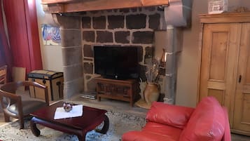 Ein Wohnzimmer mit Kamin aus Stein, einem Fernseher, einem roten Ledersofa, einem Holztisch und einem roten Sessel.