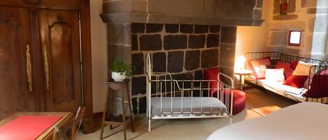 A room with a stone fireplace, a bed, a desk with a chair, and a small table with a plant.
