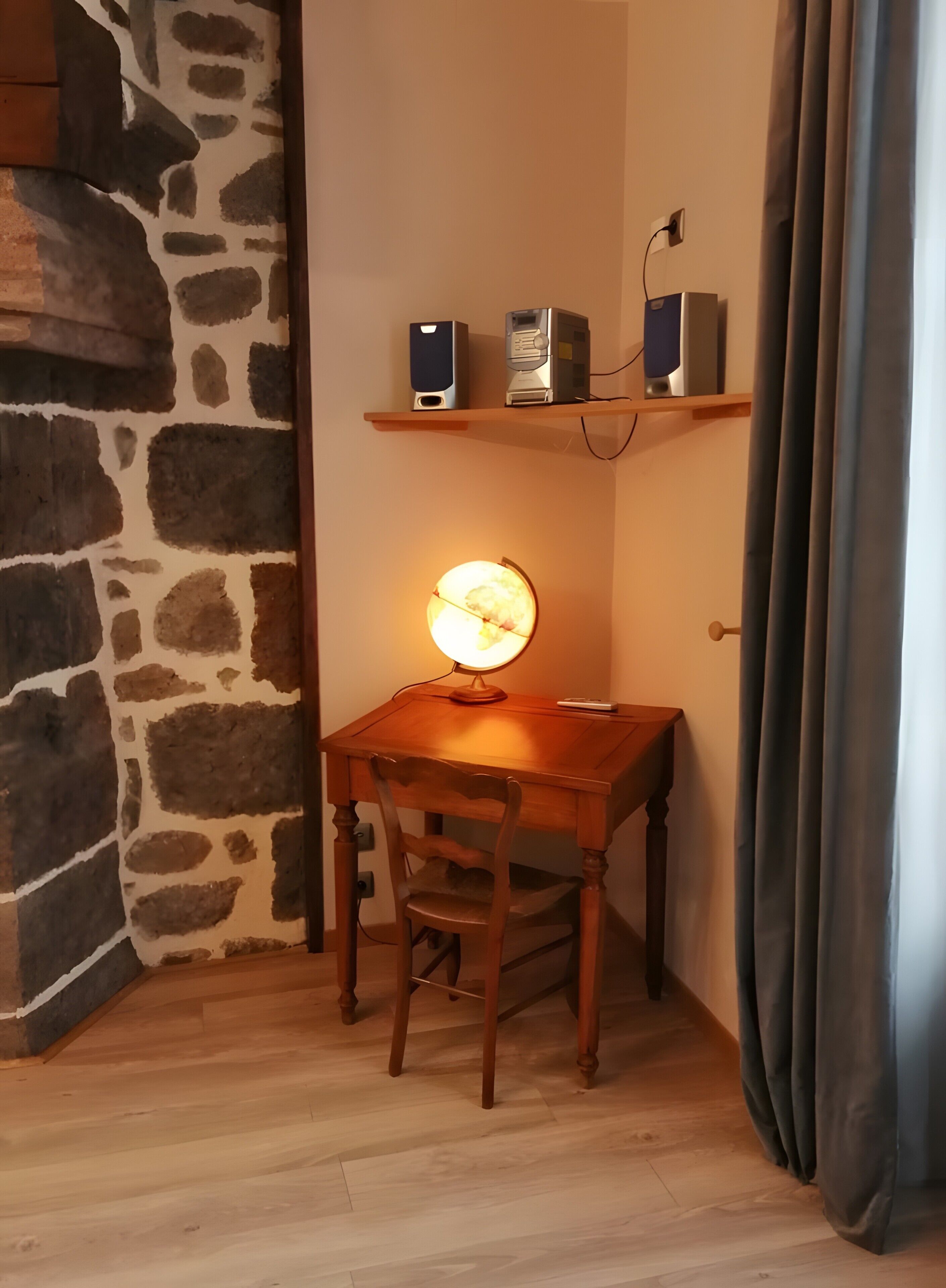 Een kamer met een houten bureau, een stenen muur, een plank met elektronische apparaten en een brandende lamp.