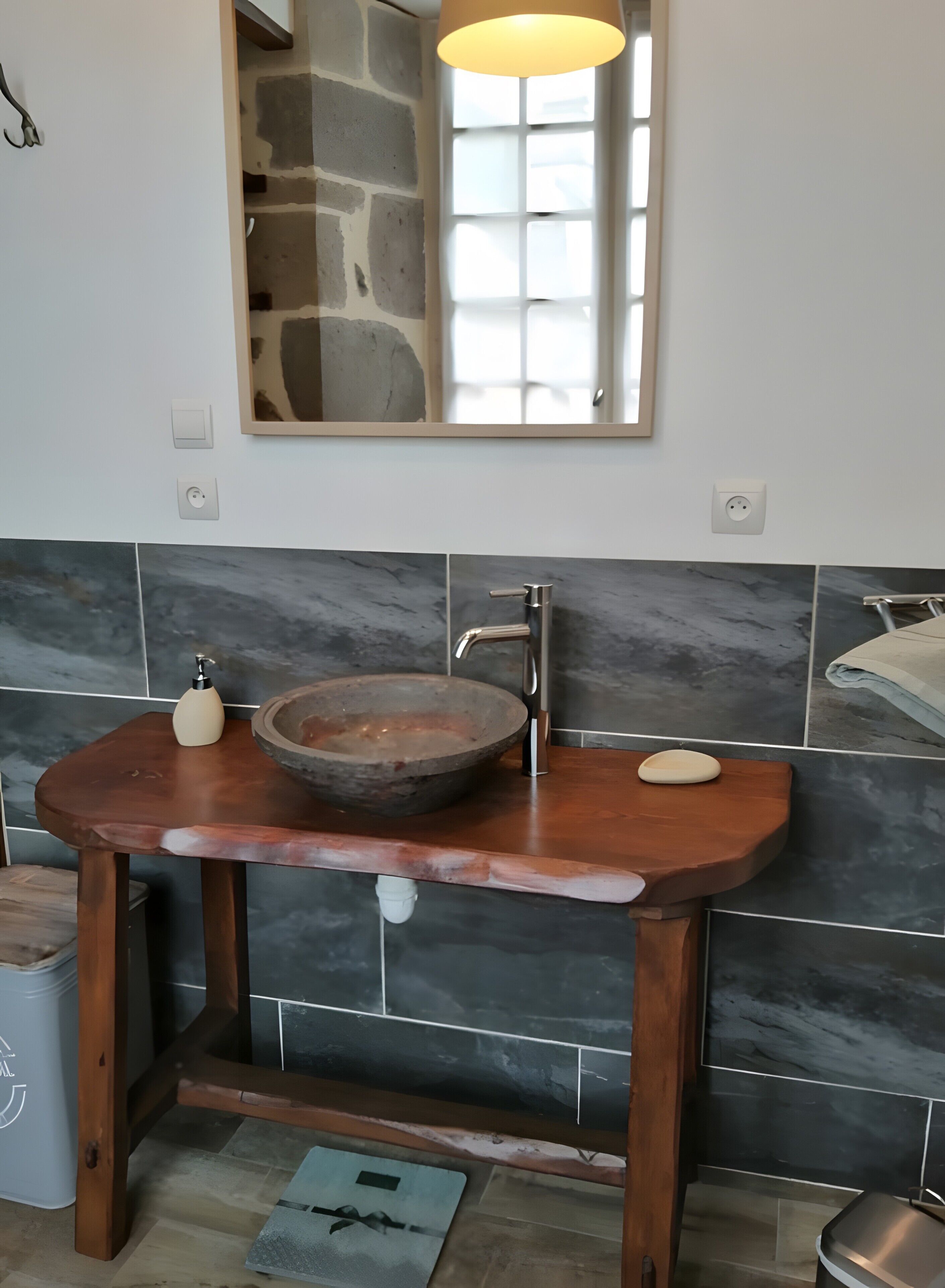A bathroom with a wooden vanity, a stone basin, a modern faucet, a mirror, and a towel rack.