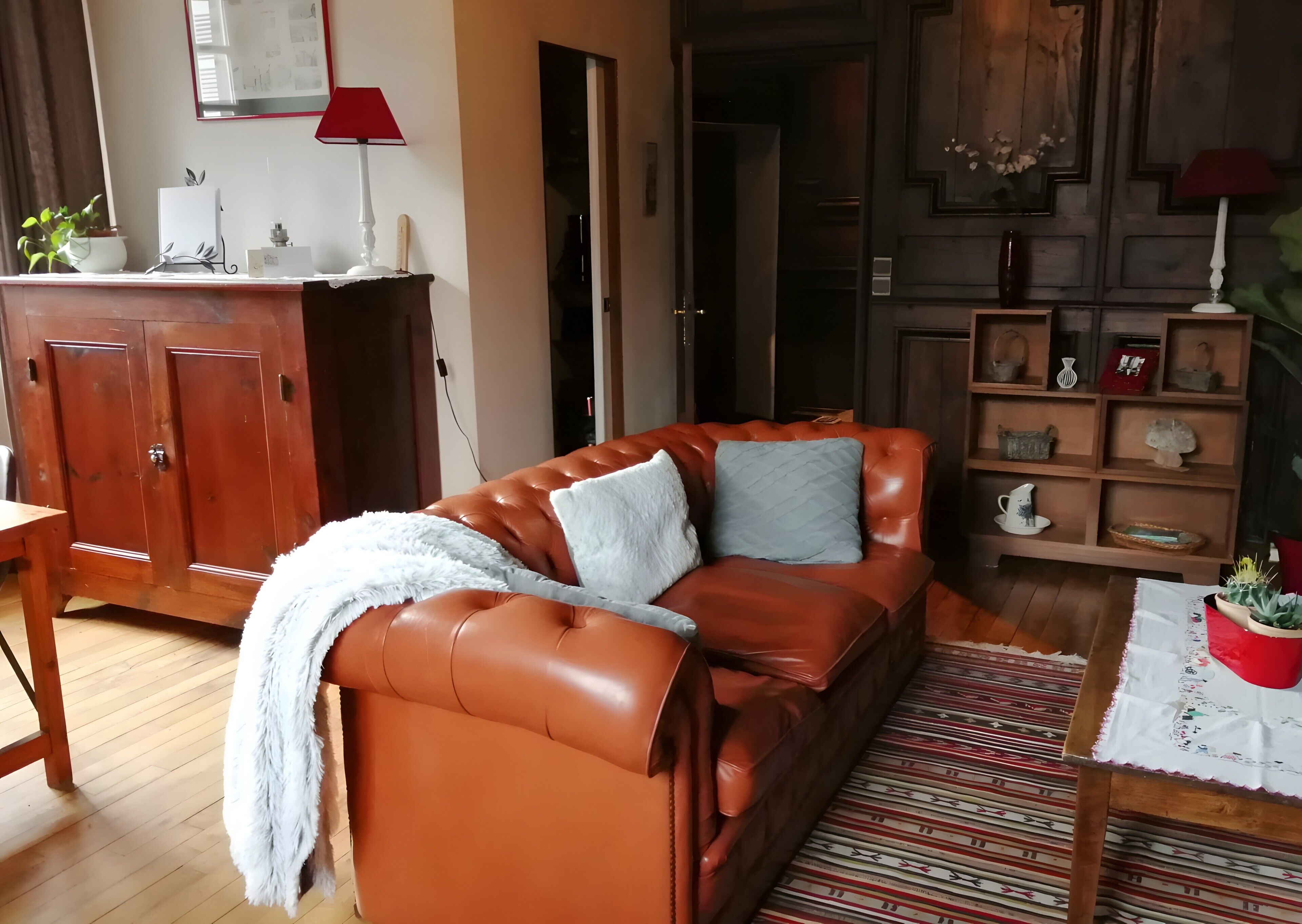 Een woonkamer met een leren bank, een houten kast, een rode lamp en een kamerkleed met dessin.
