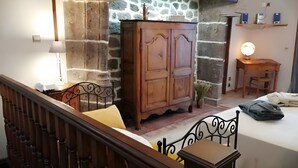 A room with a wooden wardrobe, a bed, a desk with a lamp, and a chair.