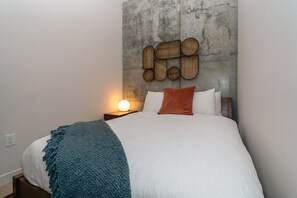 A bed with a white comforter, a teal throw blanket, and a wooden headboard with a woven design. - *NEW Mid-Century Modern 2B/1B (Halifax)