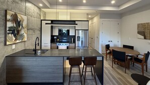 A modern kitchen with a central island, a dining area with a round table, and a large abstract painting on the wall. - Mid-Century Modern 2B/1B (Halifax)