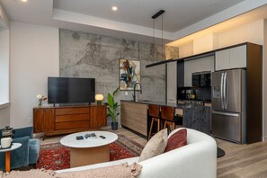 A modern living room with a flat-screen TV, a sofa, a coffee table, and a kitchen area with a refrigerator and microwave. - *NEW Mid-Century Modern 2B/1B (Halifax)