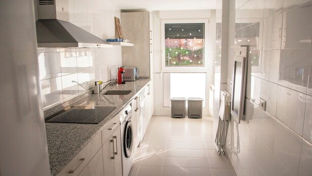 A modern kitchen with white cabinetry, a built-in oven, a microwave, and a stainless steel range hood. - VERARLANZA LERMA BURGOS (Lerma)
