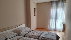 A bedroom with two beds, a window with sheer curtains, and a radiator. - VERARLANZA LERMA BURGOS (Lerma)