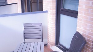 A small outdoor patio with a metal table and two chairs, a brick wall, and a window with a view. - VERARLANZA LERMA BURGOS (Lerma)