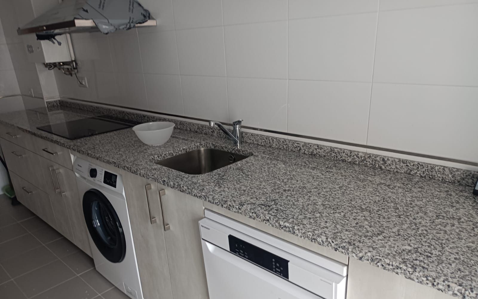 Een praktische keuken met een ingebouwde wasmachine, een vaatwasser en een granieten aanrecht.