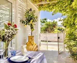 An outdoor dining area with a table set for two, a vase with flowers, and a potted plant.