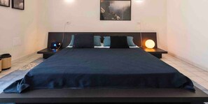 A modern bedroom with a large bed, bedside tables, a wall-mounted TV, and a painting.
