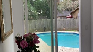 A room with a view of a backyard swimming pool, a vase with flowers on a table, and a pair of shoes on a rug.
