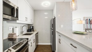 A modern kitchen with stainless steel appliances, white cabinetry, and a wooden floor.