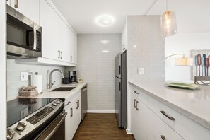 A modern kitchen with stainless steel appliances, white cabinetry, and a wooden floor. - Upgraded Corner Unit with Amazing Pool and Ocean Views! - Sugar Beach #421 (Kihei, Maui)