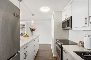 Une cuisine moderne avec des meubles blancs, un réfrigérateur en acier inoxydable, un four à micro-ondes et une plaque de cuisson noire.