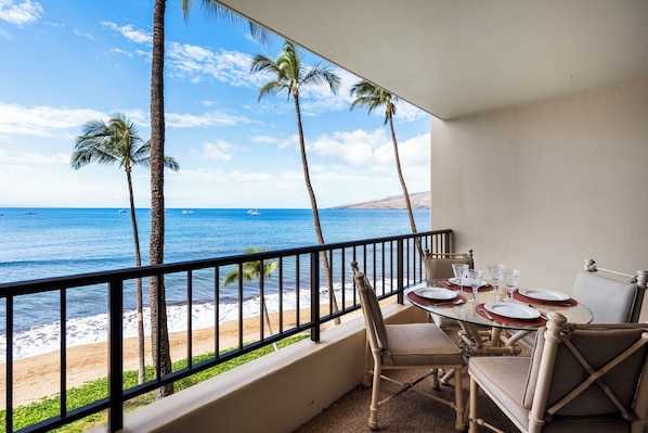 Un balcon avec une table dressée pour le dîner, donnant sur une plage bordée de palmiers et sur l’océan.