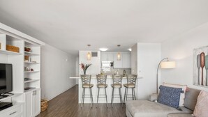 A modern living room with a grey sectional sofa, a TV, and a kitchen area with a bar stool set.
