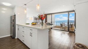 A modern kitchen with white cabinets, a stainless steel refrigerator, and a large island with a fruit bowl and vase.