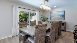 A dining area with a large table, wicker chairs, a chandelier, and a view of the outdoors. - 15 Wagon Road: Walk to the beach! Private Pool with Lagoon View! (Hilton Head Island)