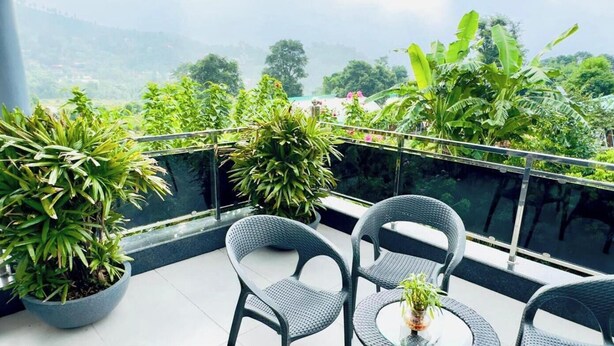 Un balcon agrémenté de deux fauteuils en osier et d’une petite table, entouré de plantes en pot et offrant une vue sur un paysage luxuriant.