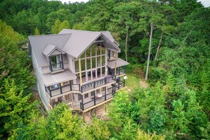 Ein großes, mehrgeschossiges Haus mit einem auffälligen Balkon, umgeben von dichtem Wald.