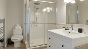 Et moderne badeværelse med et brusekabine i glas, et hvidt toilet og en vask med spejl.