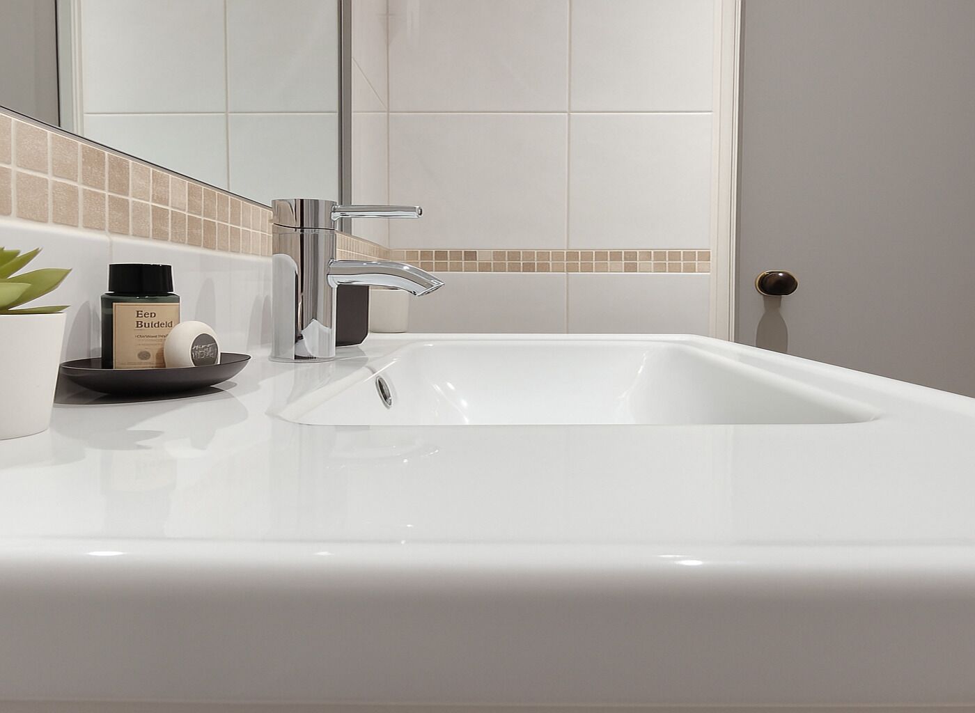 A modern bathroom with a white sink, chrome faucet, and a small potted plant.