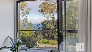 A room with a large sliding glass door leading to a balcony with a view of trees and a body of water.