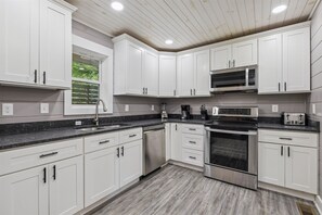 A modern kitchen with white cabinets, stainless steel appliances, and a granite countertop. - Amazing Views Hot Tub Arcade Firepit (Gatlinburg)