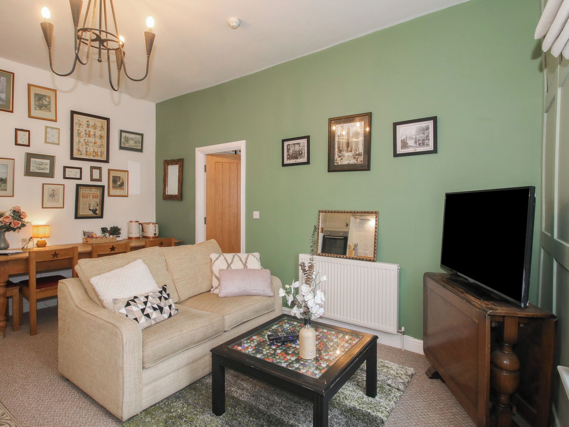 A living room with a sofa, coffee table, and a television. There are framed pictures on the wall and a chandelier.