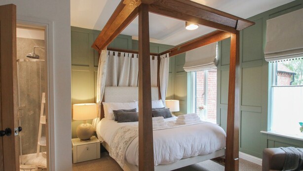 Un dormitorio con cama con dosel, una mesita de noche con lámpara y una ventana con persianas.