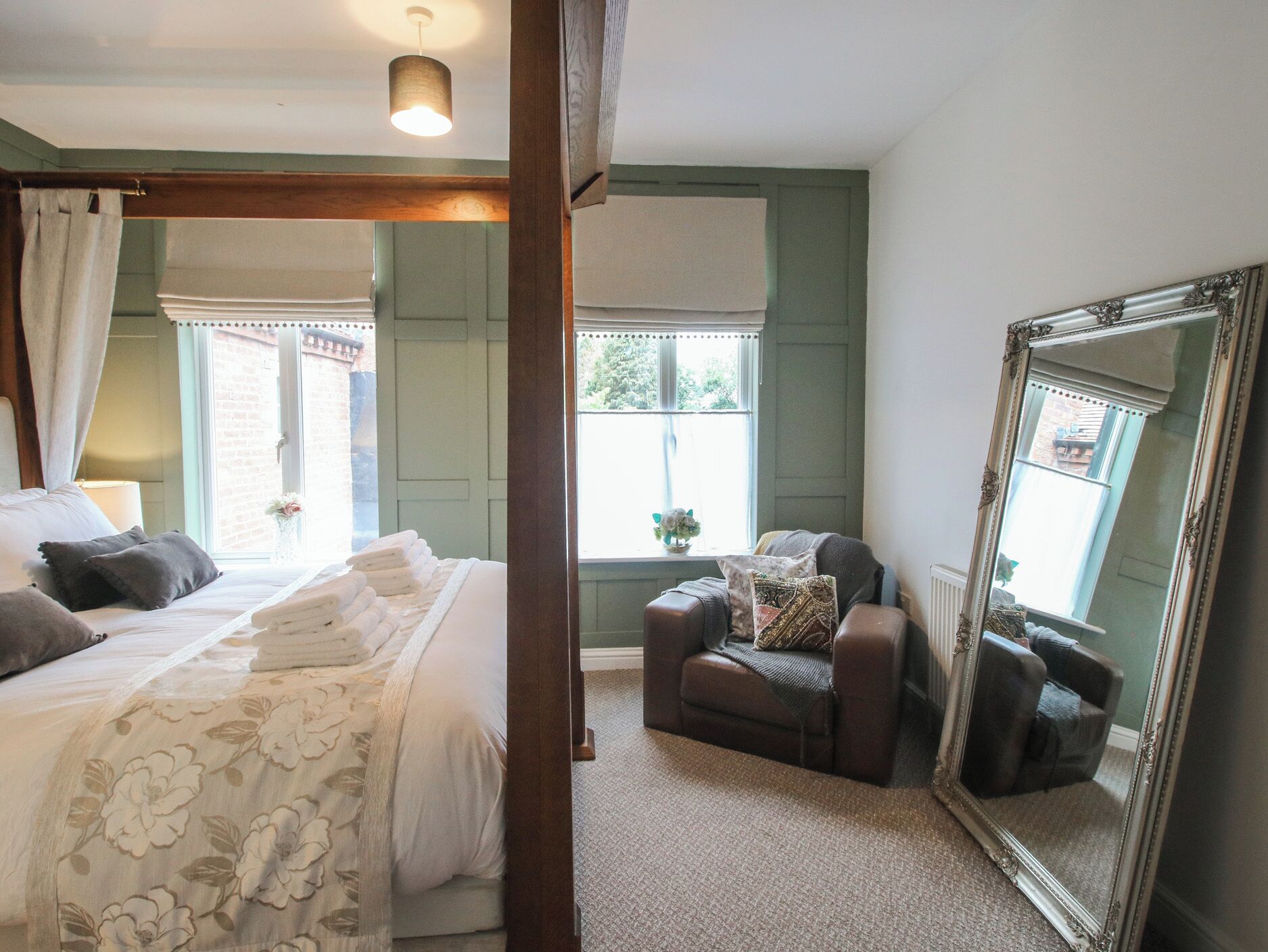 A bedroom with a large bed, a chair, a mirror, and a window with curtains.
