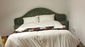 A bed with a green upholstered headboard, white bedding, and a patterned throw.