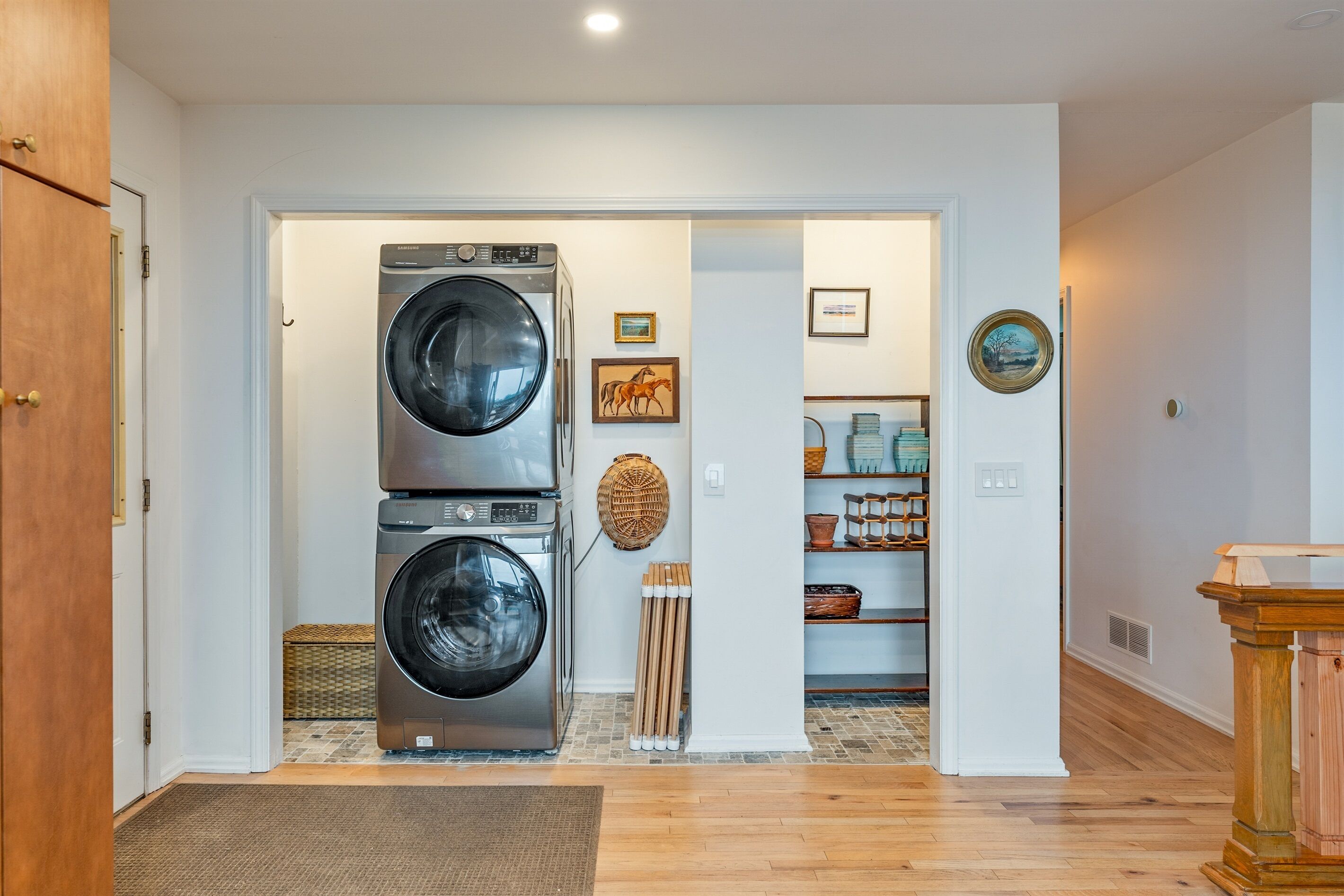 A laundry room with two stacked front-loading washers and dryers, a wicker basket, and a wooden bench.