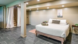 Une chambre à coucher avec un lit, une table de chevet, un tableau accroché au mur, un escalier agrémenté de rideaux et une porte.