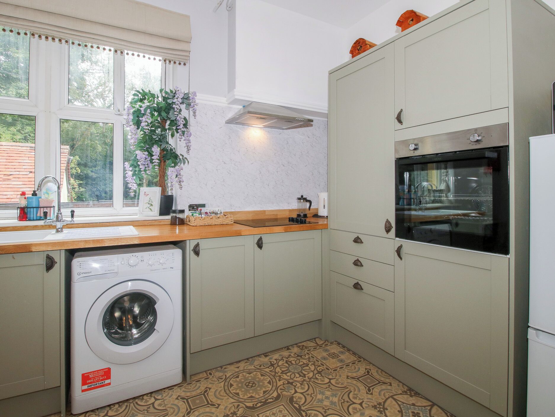 A compact kitchen with a washing machine, a built-in oven, and a window with a view of greenery.