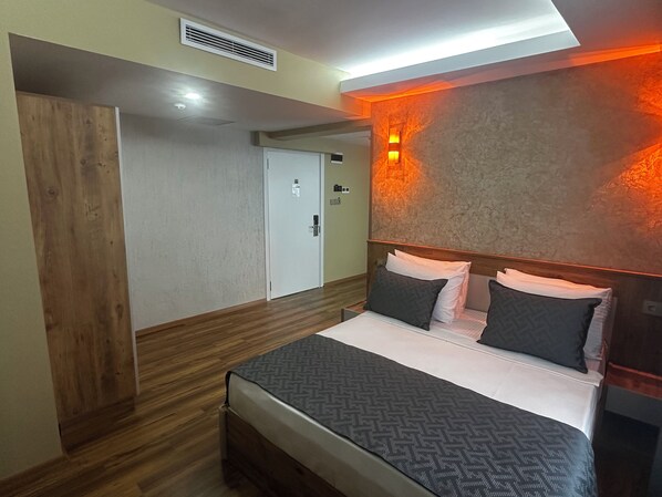 Un dormitorio con suelo de madera, una cama con ropa de cama estampada, una lámpara de pared y una puerta.