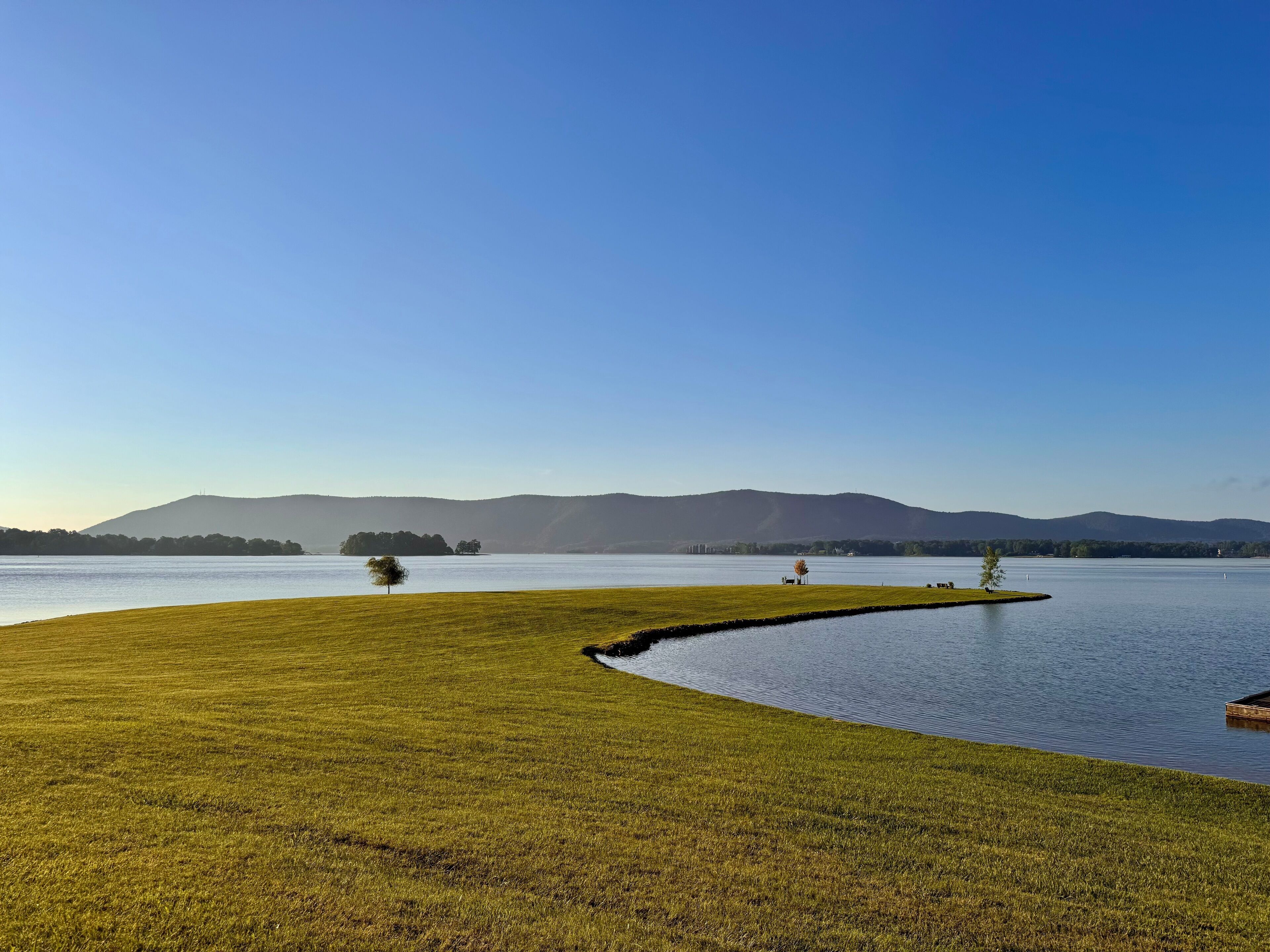 A serene lakeside landscape with a grassy area, a curved water path, and distant hills.