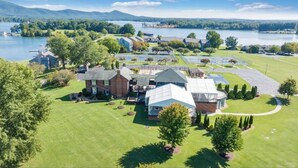 Une grande maison avec une vaste pelouse, un court de tennis et un lac en arrière-plan.