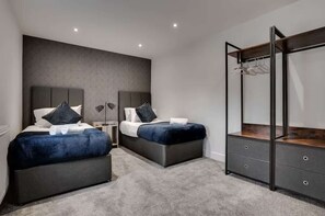 A modern bedroom with two beds, a wardrobe, and a large mirror. - Victoria Place (Hyde)