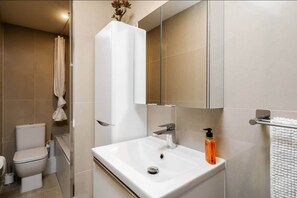 A modern bathroom with a white sink, a toilet, and a shower area. - Victoria Place (Hyde)
